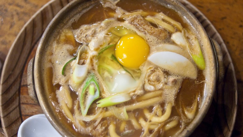 A large, ceramic bowl of miso nikomi udon from above, plated with a white ladle-style spoon.