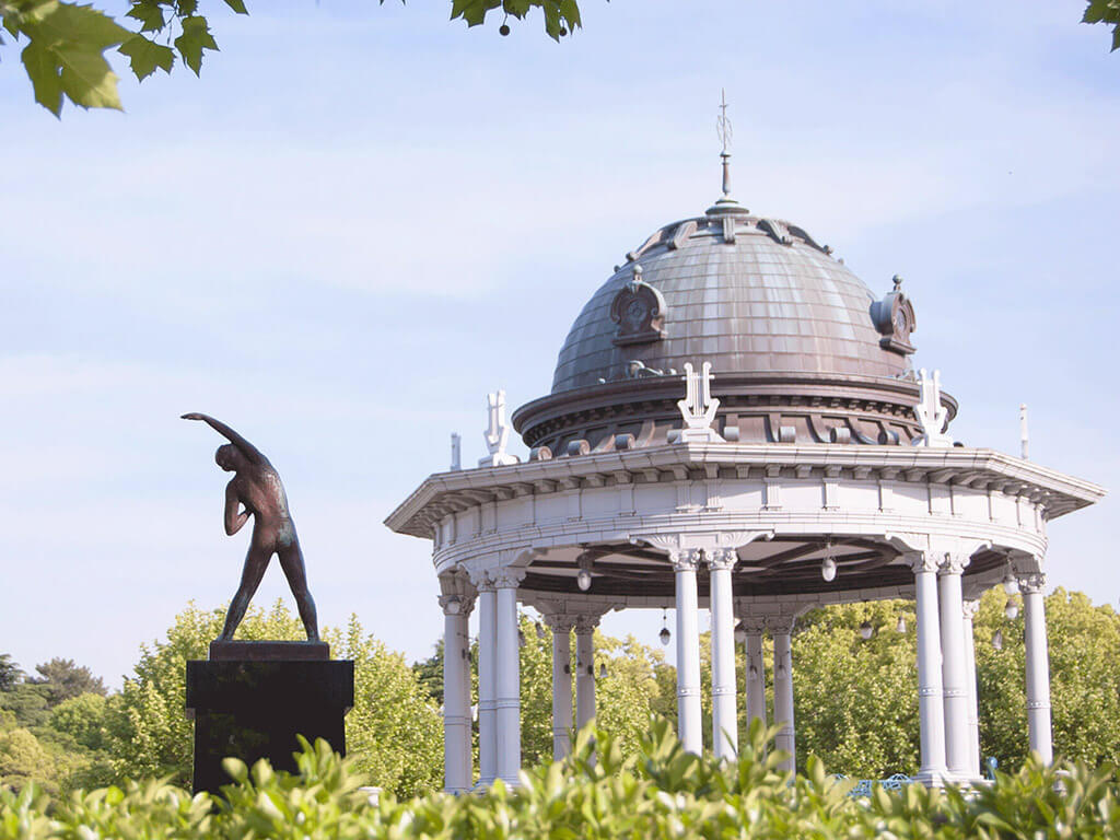 A stretching statue and gazebo surrounded by green at Tsurumai Park.