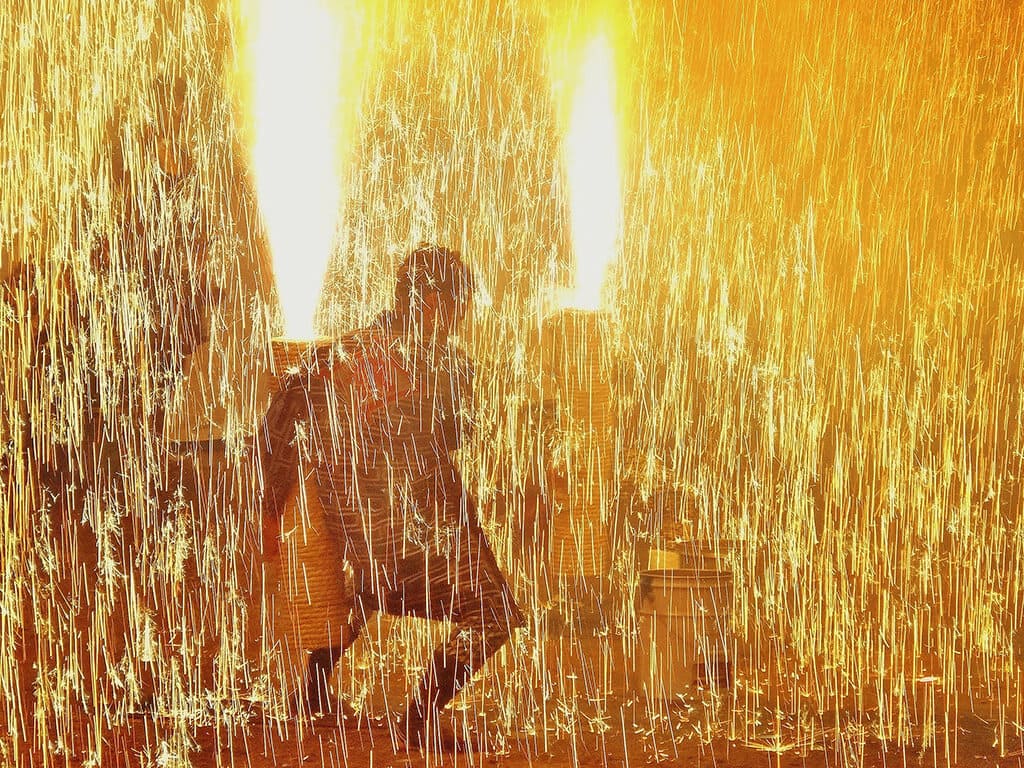 Performers shooting the handheld fireworks blazing all around them in a yellow-orange light.