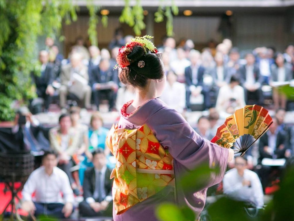 A Geisha performing in front of a crowd with her Sensu (hand fan). Image via Ryotei Kawabun.