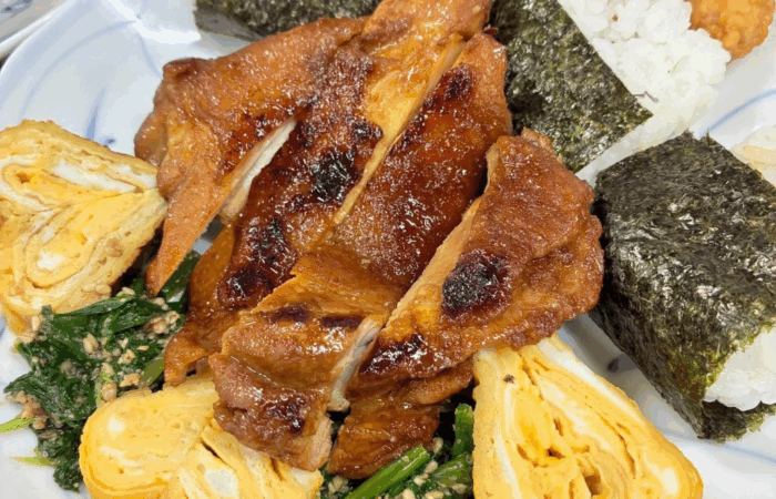 Tebasaki chicken wings on a bed of sesame spinach, heart-shaped rolled egg omelet, and shrimp tenmusu onigiri.