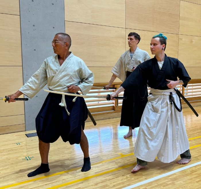 Inuyama Iaido Lesson with the instructor and two people dressed in black and white hakama, mid-draw.