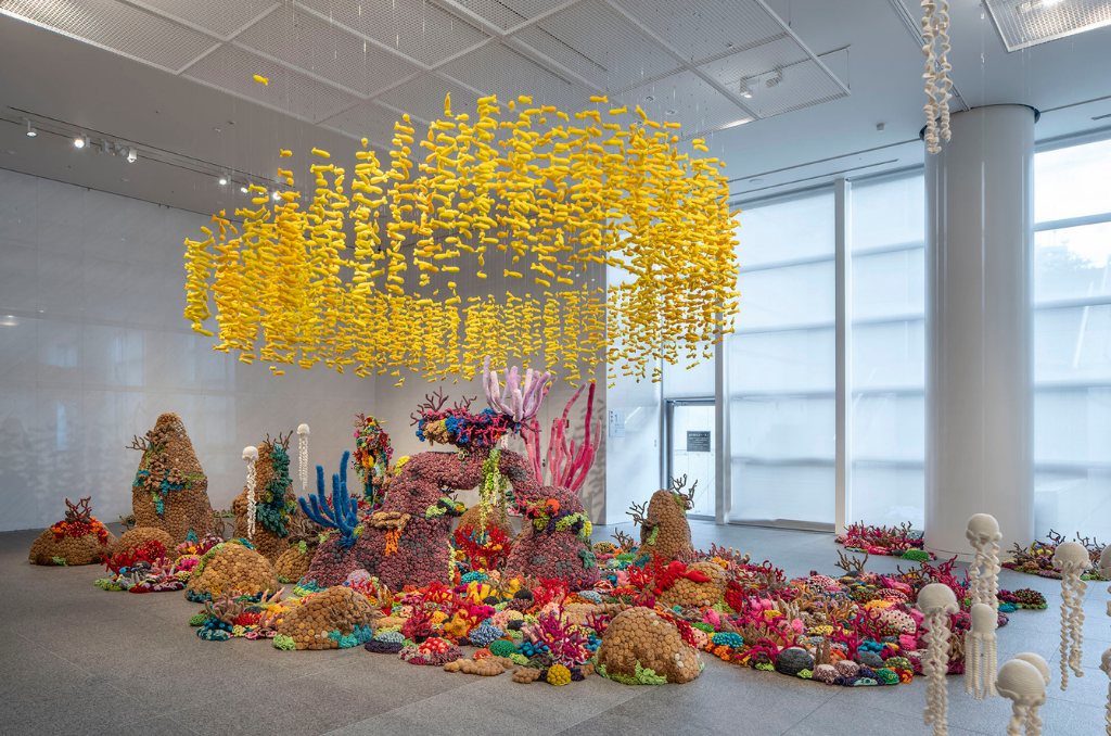 A colorful exhibit modeled after a coral reef. Yellow fish and white jellyfish hang from the ceiling on invisible strings, and the reef structure spreads out across the floor.