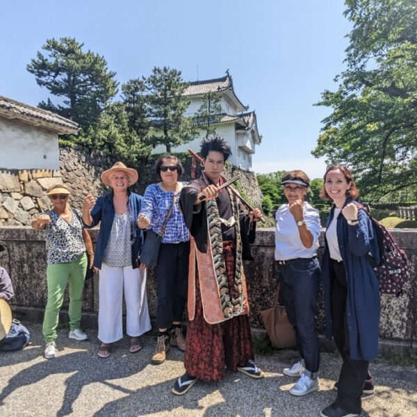 Nagoya Castle samurai A Japanese man dressed in a samurai outfit posing with guests in front of Nagoya Castle on a clear day.