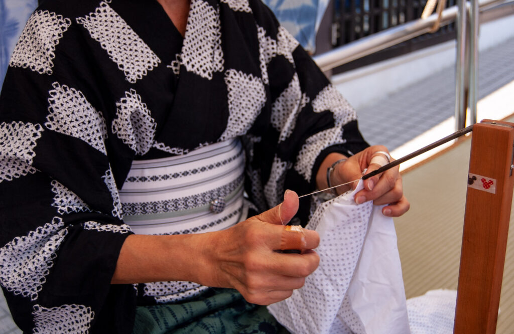 A kimono-wearing weaver works on threading a piece of fabric.