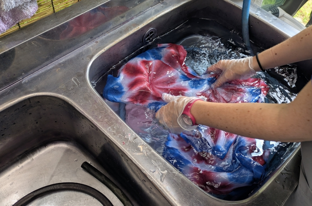 Rinsing the dyed red-and-blue fabric in the sink.