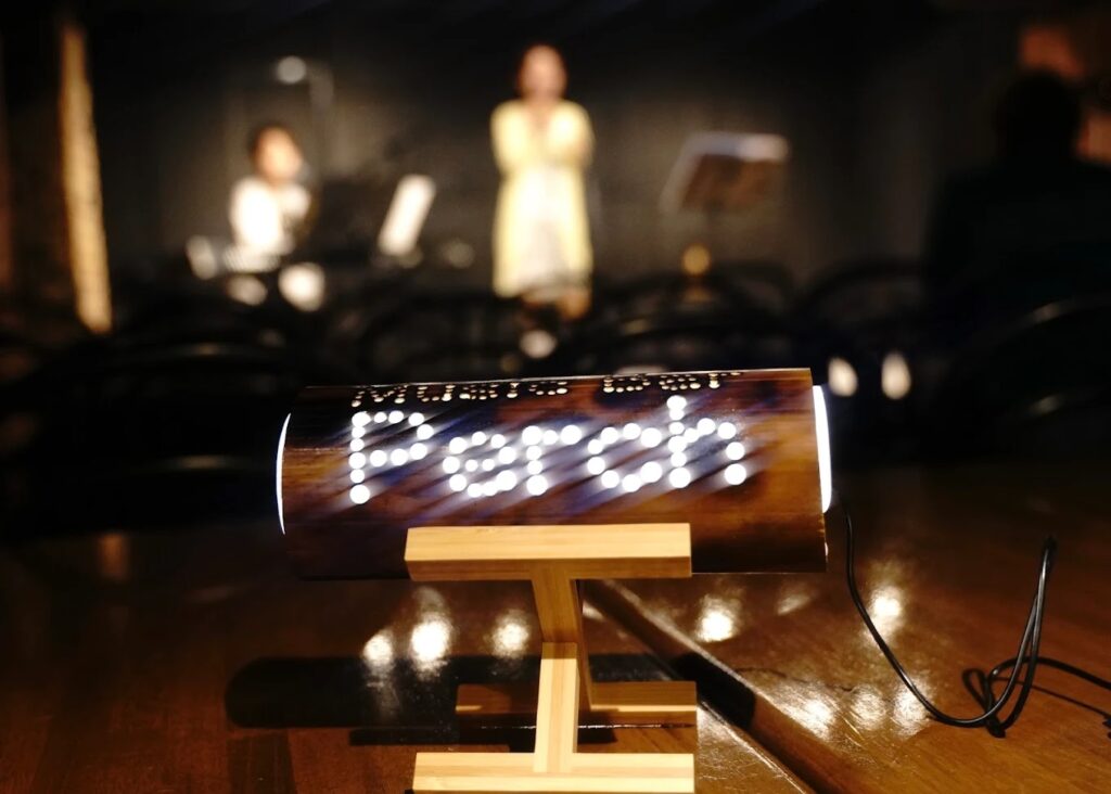 The tin light at Music Bar Perch, with the name punched out and the performers out of focus in the background.