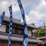 Four indigo banners fly under a cloudy sky at the Arimatsu Shibori Tie-Dye Festival.