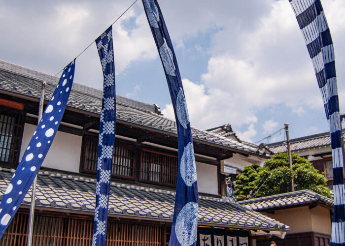 Four indigo banners fly under a cloudy sky at the Arimatsu Shibori Tie-Dye Festival.