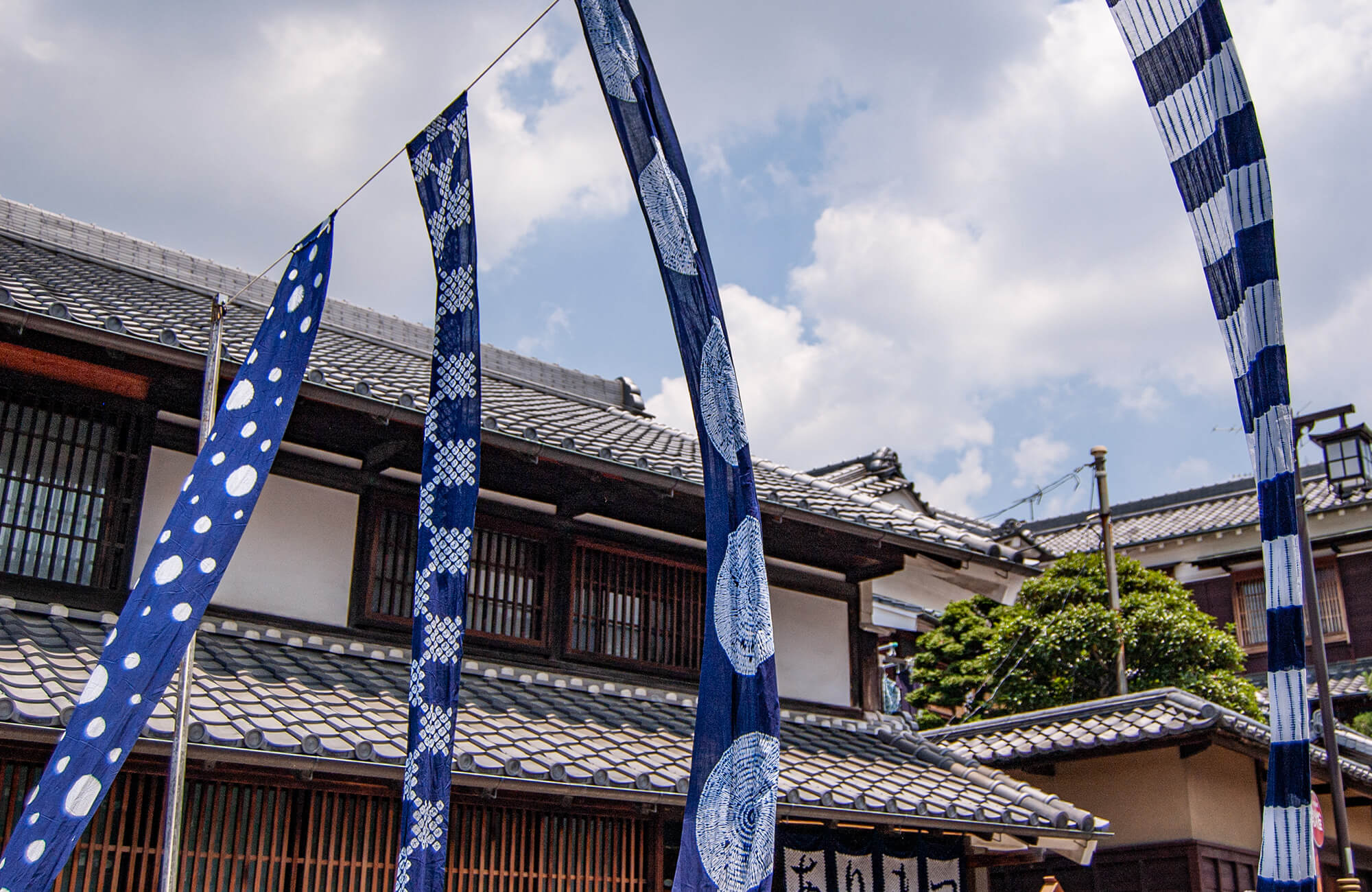 Four indigo banners fly under a cloudy sky at the Arimatsu Shibori Tie-Dye Festival.