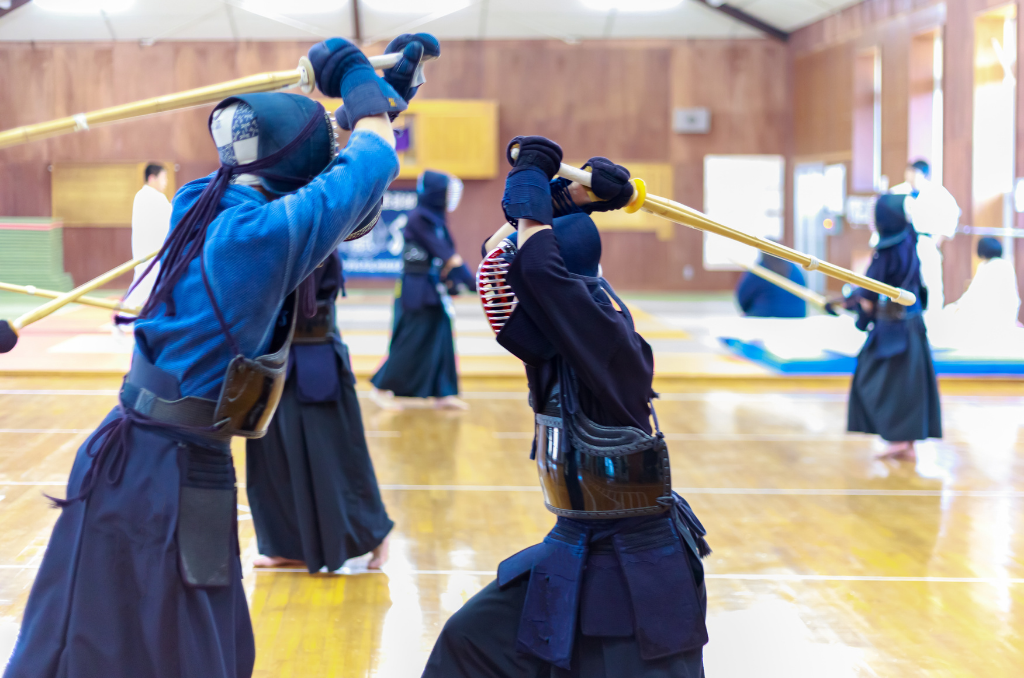 Kendo swordsmen in competition, with both swords hoisted and poised backwards above the head.