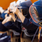 Kendo swordsmen kneeling and putting their helmets on in a line.