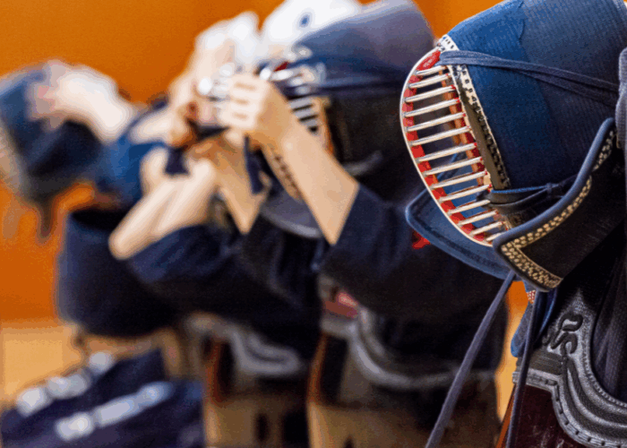 Kendo swordsmen kneeling and putting their helmets on in a line.