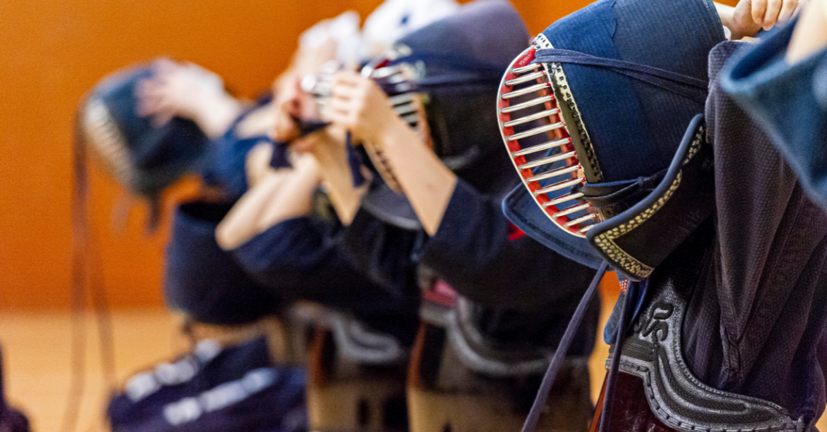 Kendo swordsmen kneeling and putting their helmets on in a line.