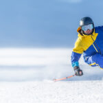 A young aggressive skier on an alpine slope demonstrates an extreme carving skiing style. He is skiing on morning perfectly groomed piste.