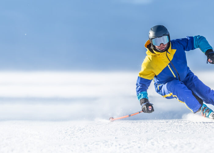 A young aggressive skier on an alpine slope demonstrates an extreme carving skiing style. He is skiing on morning perfectly groomed piste.