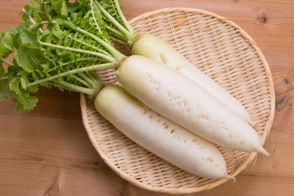Three daikon radishes set on a woven bamboo plate shot from above.