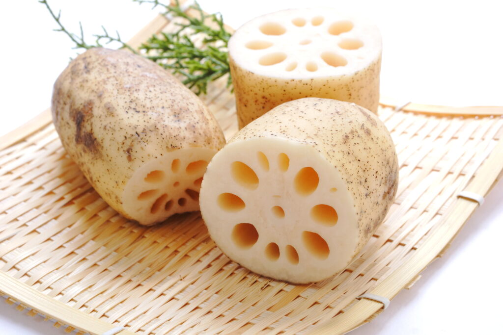 Three chunks of lotus root cut open to display the webbed texture on a woven bamboo plate.