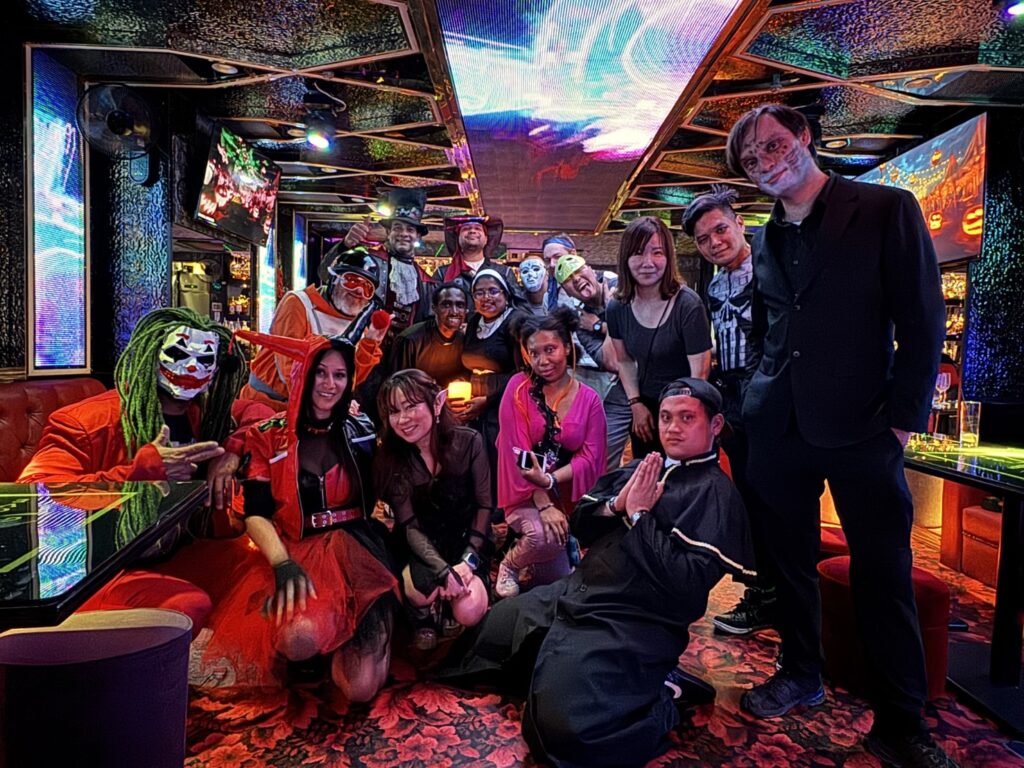 Participants dressed up in Halloween costumes smiling and posing for the camera in a colorful club room.