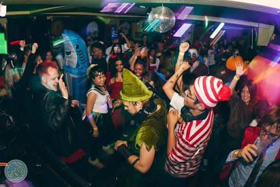 Partygoers dressed up in Halloween costumes dance the night away amid strobe lights and a DJ.